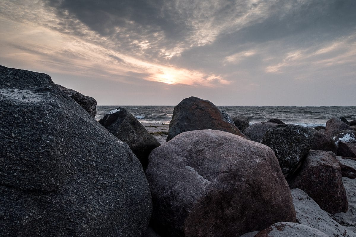 Große Felsen am Strand mit Meer im Hintergrund unter einem bewölkten Himmel bei Sonnenuntergang