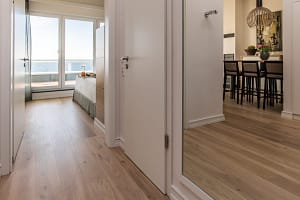 Blick durch einen Flur mit Holzboden zu einem Schlafzimmer mit Meerblick und einem Esstisch mit hohen Stühlen und Dekoration im Hintergrund.
