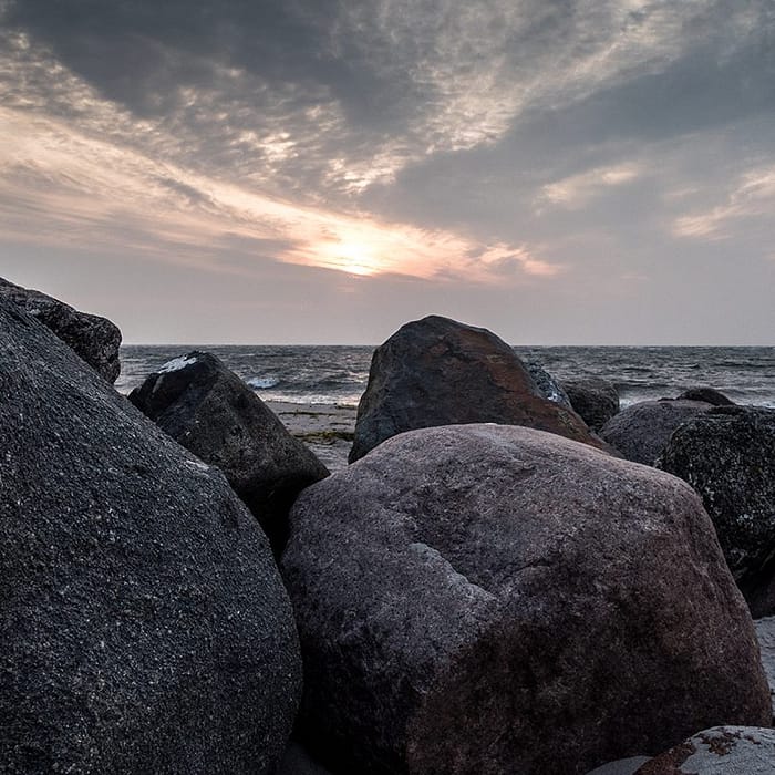 Große Felsen am Strand mit Meer im Hintergrund unter einem bewölkten Himmel bei Sonnenuntergang